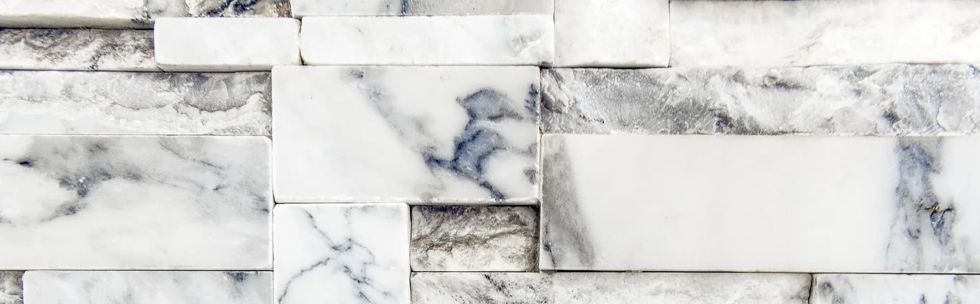 Close-up of a white marble mosaic wall with grey veining running through irregular block joints