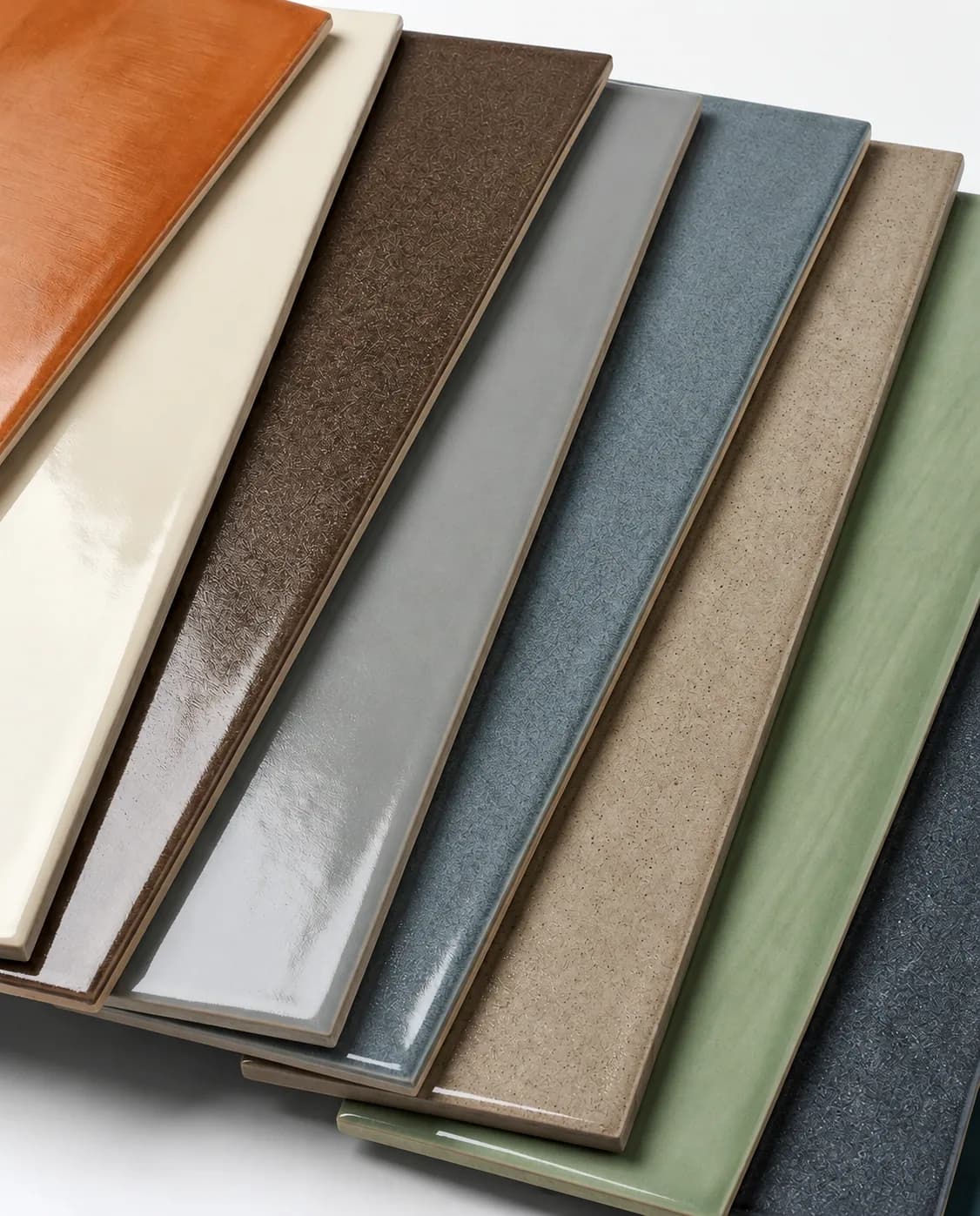 Baton tiles fanned across each other in amber, cream, brown, grey, teal, sand, sage and charcoal, showing gloss, crackle and speckled glazes side by side