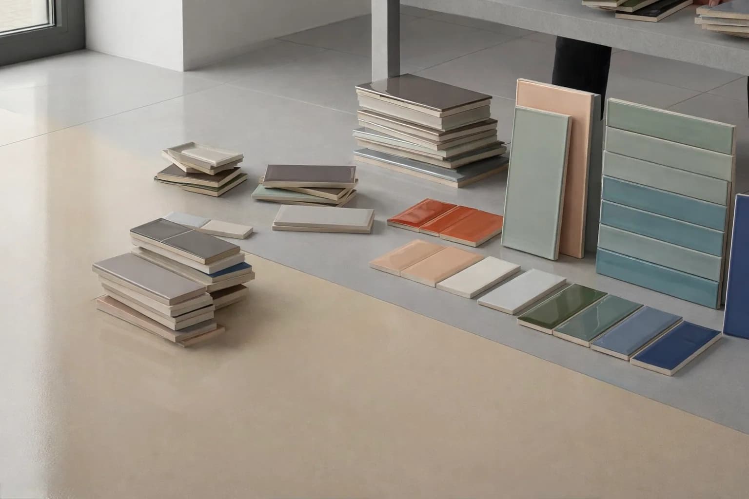 Glossy subway tiles in blush, sage, teal, olive and blue, stacked and fanned out across a showroom floor