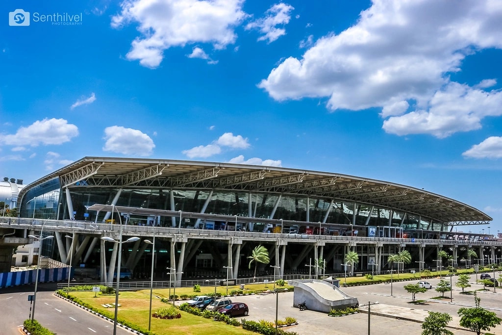 The curved steel and glass terminal of Chennai International Airport seen from the approach road under a bright sky