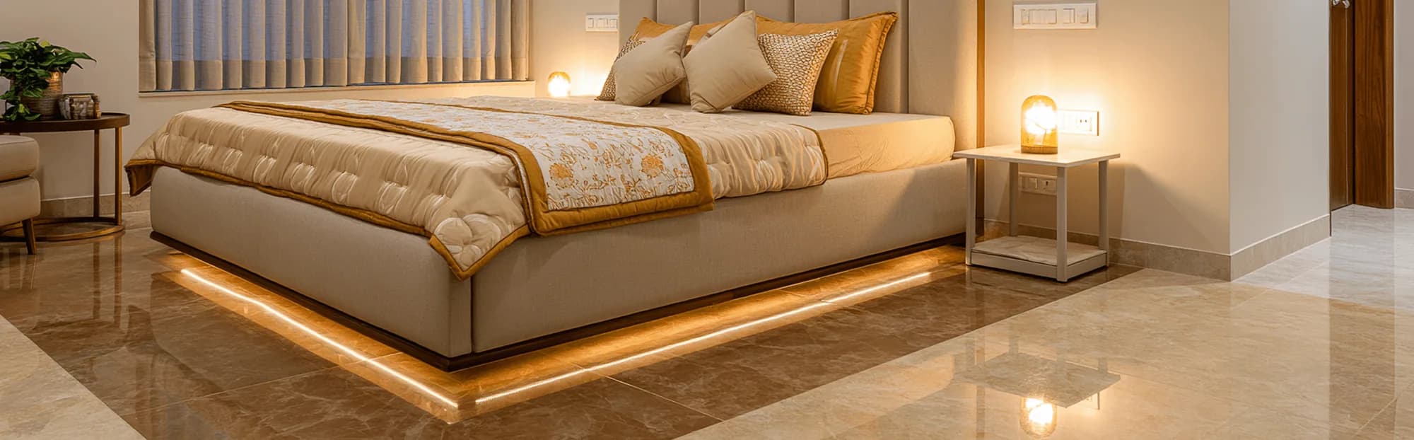 Close crop of a bedroom floor in glossy warm caramel-gold marble-look tile, beside a backlit bed base