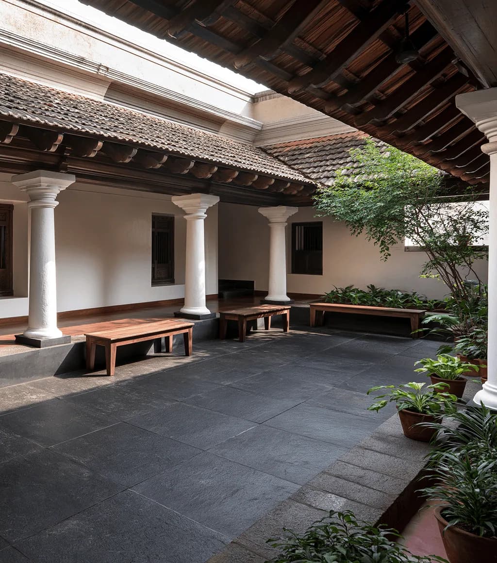 Traditional colonnaded courtyard floored in dark grey-black Kadappa stone, with white columns and a tiled roof