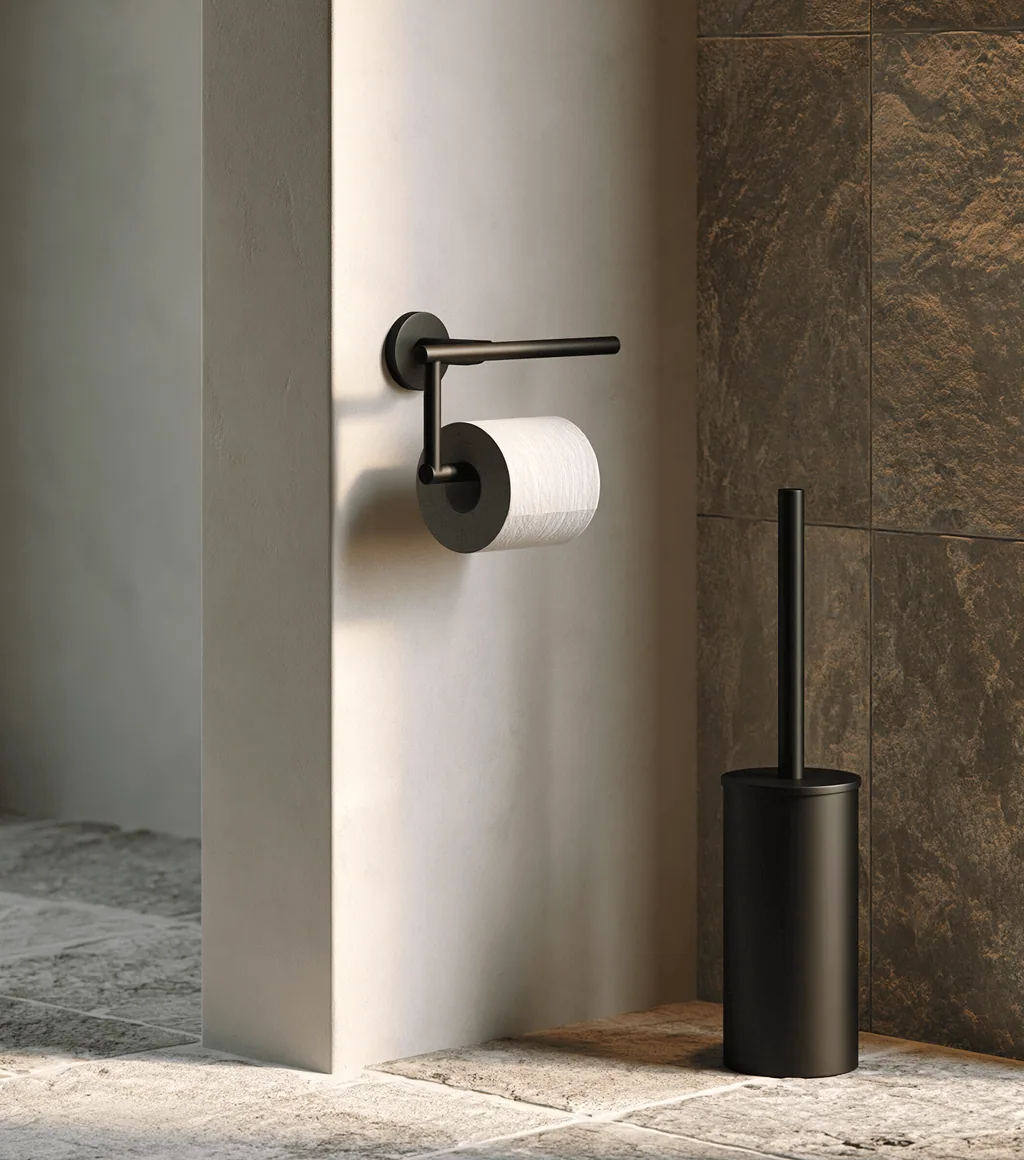 Matte black toilet-roll holder and freestanding toilet brush against a stone-clad wall