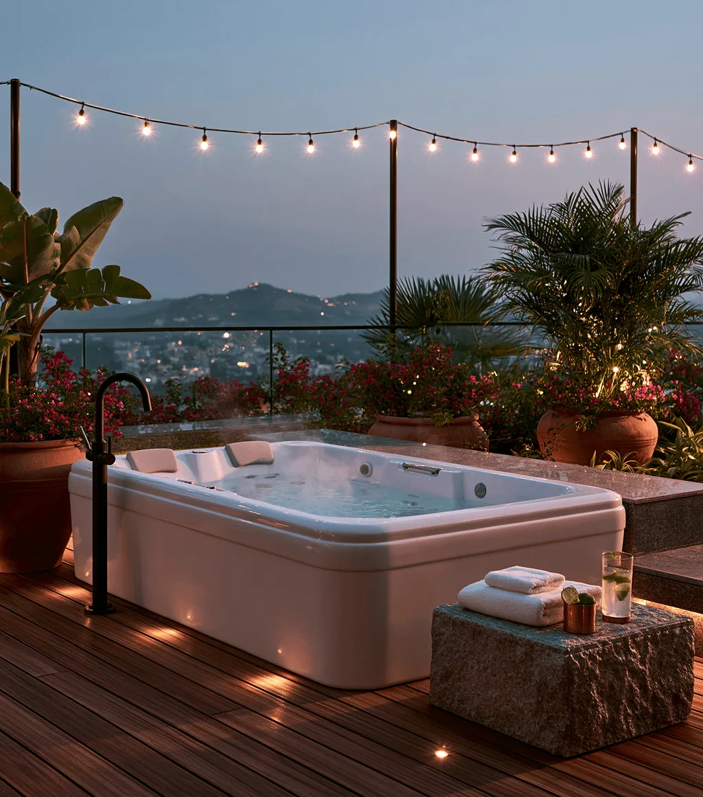 White multi-jet spa tub on a rooftop deck at dusk, with a black floor-mounted faucet and string lights