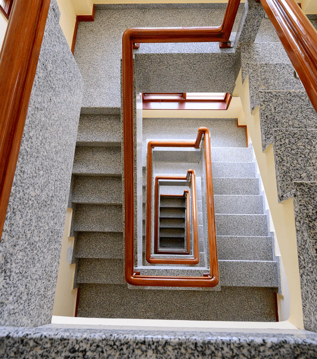 Spiral stairwell viewed from above, treads and walls clad in grey speckled granite