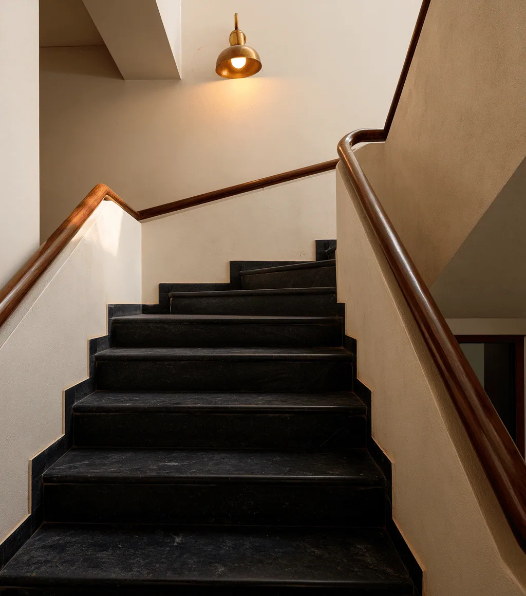 Staircase with dark honed black Kota-stone treads, beside a brass wall sconce