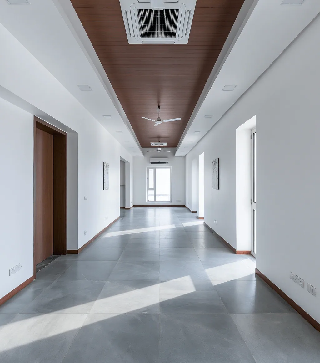 Long corridor floored in grey honed Kota-look large-format tile, beneath a wood-panelled ceiling