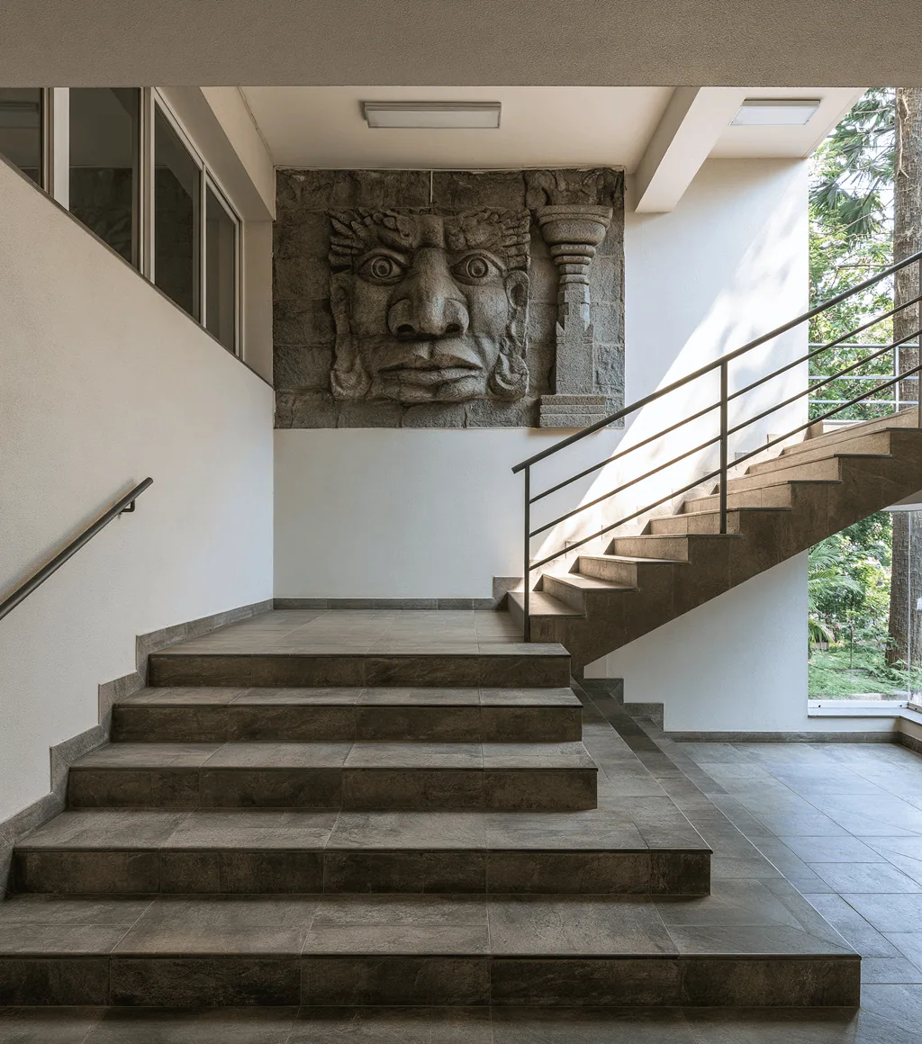 Office stairwell in dark grey stone-look large-format floor tile, beside a decorative carved wall panel