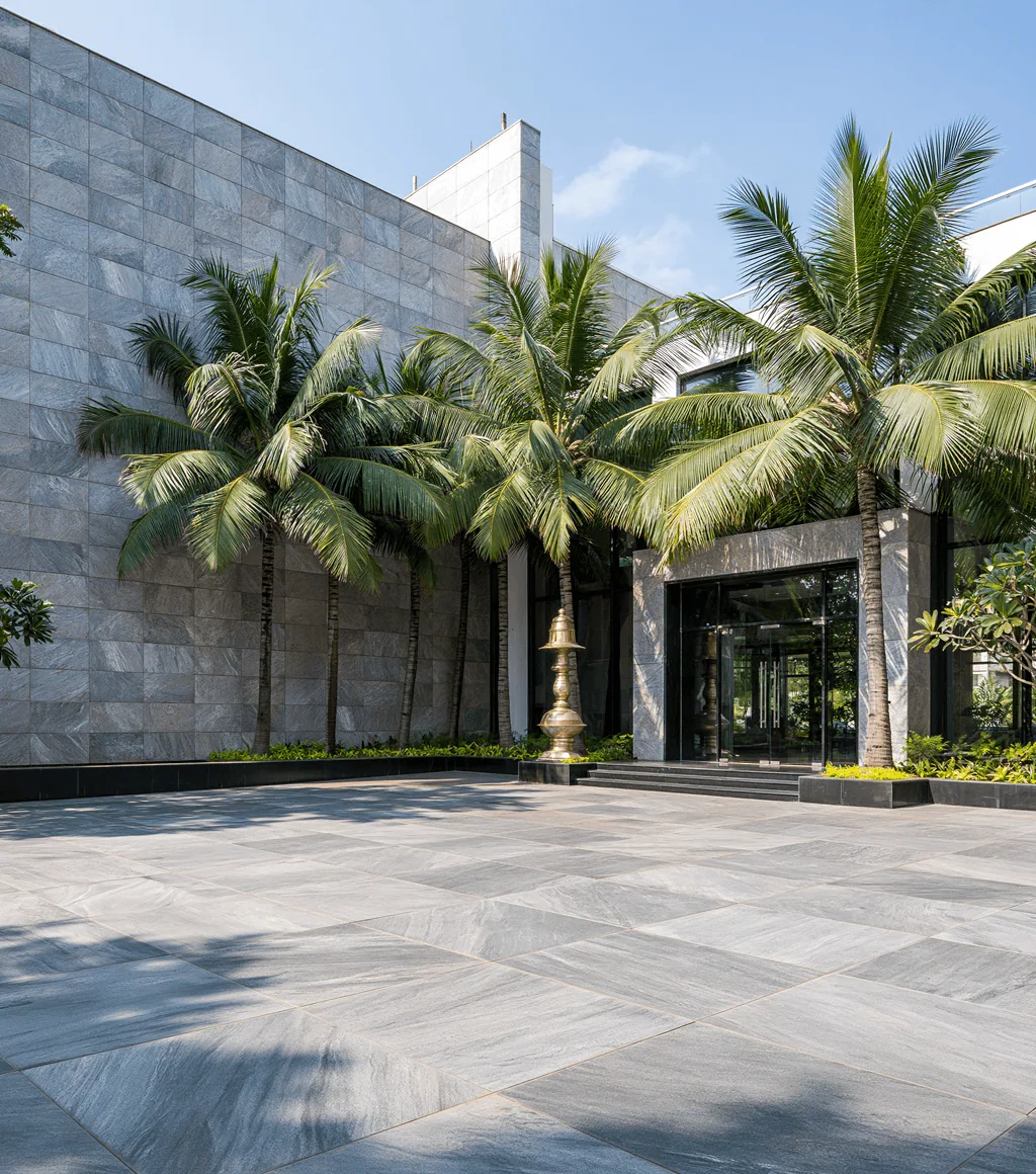 Office building forecourt in grey stone-look paving, with a glass entrance framed by palm trees